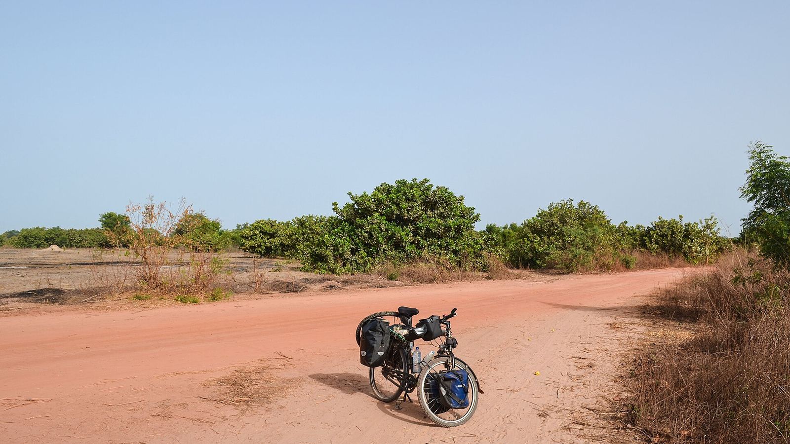 Touring bicycle with panniers on a red sand track through scrub, The Gambia