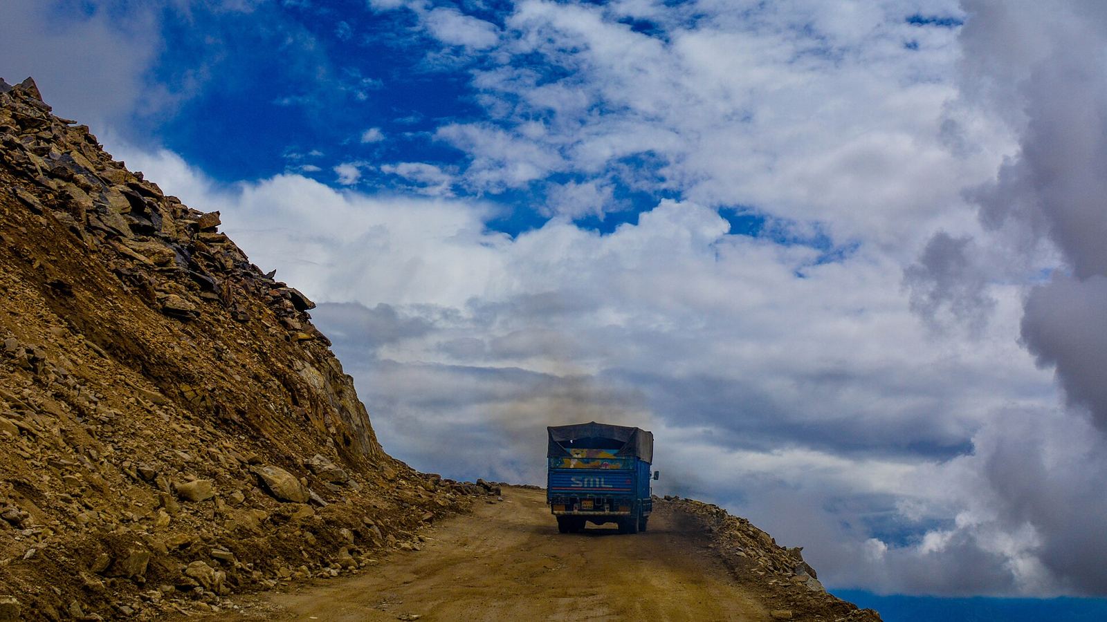 Truck on a dirt mountain road near Khardung La, Ladakh, under a dramatic blue sky
