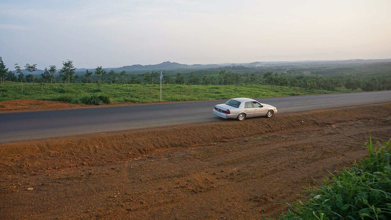 Highway between Monrovia and Gbarnga with a car on the road, red earth in the foreground
