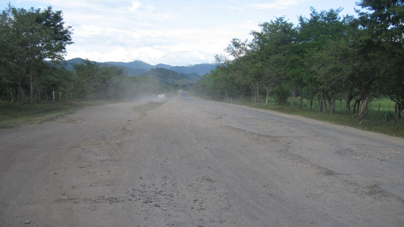 Dirt road to El Sauce with a car raising dust and hills in the distance