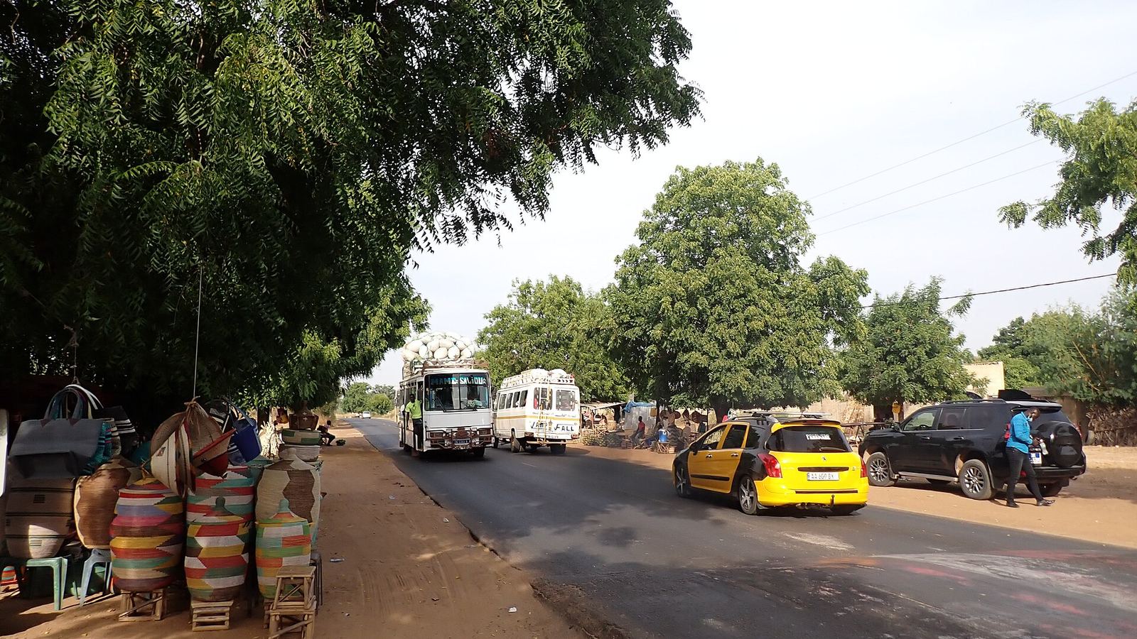 Road at Mboro towards Tivaouane with buses, a taxi and a basket stall, Senegal